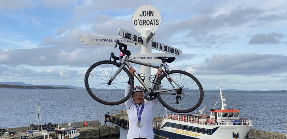 Alison holding her bike up at John O'Groats sign