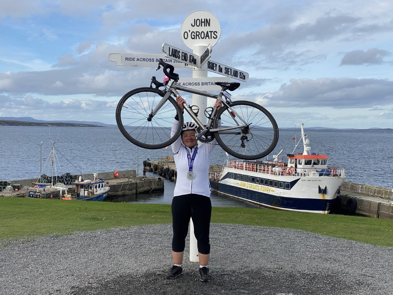 Alison holding her bike overhead at the John O'Groats sign